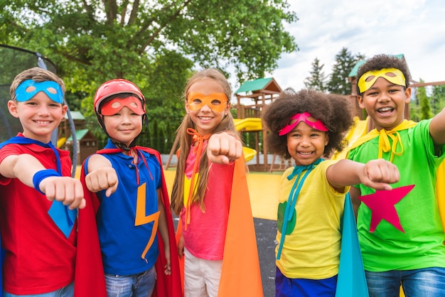 Groupe multiracial de jeunes écoliers portant des costumes de super-héros et s'amusant à l'extérieur