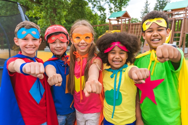 Groupe multiracial de jeunes écoliers portant des costumes de super-héros et s'amusant à l'extérieur