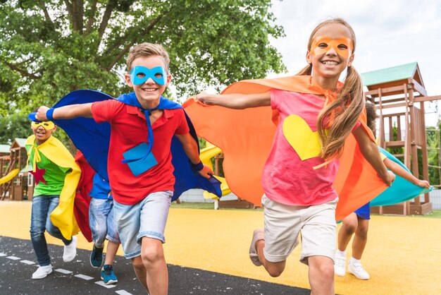 Groupe multiracial de jeunes écoliers portant des costumes de super-héros et s'amusant à l'extérieur