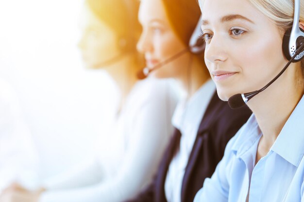 Groupe d'opérateurs téléphoniques divers au travail dans un bureau ensoleillé. Belle femme d'affaires avec un casque consultant les clients. Concept de centre d'appels et de gens d'affaires.