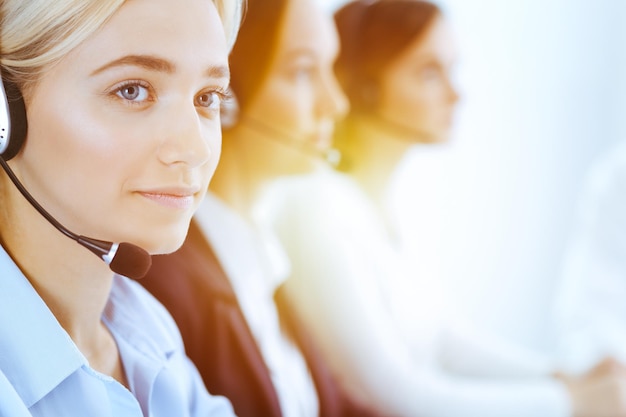 Groupe d'opérateurs téléphoniques divers au travail dans un bureau ensoleillé. Belle femme d'affaires avec un casque consultant les clients. Concept de centre d'appels et de gens d'affaires.