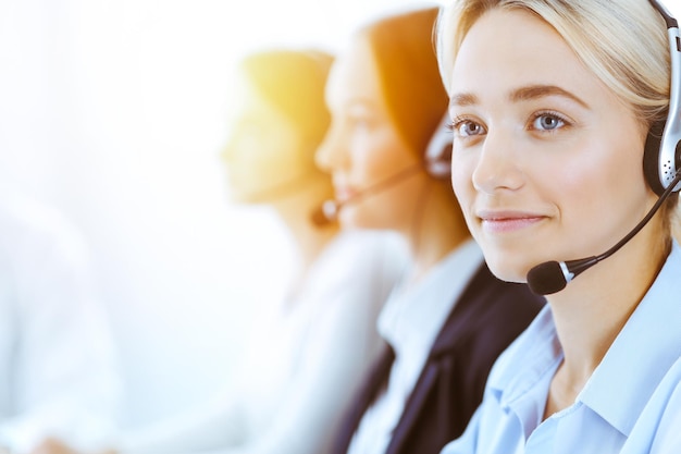 Un groupe d'opérateurs téléphoniques divers au travail dans un bureau ensoleillé. Une belle femme d'affaires avec des écouteurs consultant des clients. Le concept de centre d'appels et de gens d'affaires.