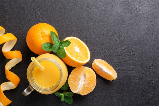 Un groupe d'oranges et un verre de jus sur une table sombre