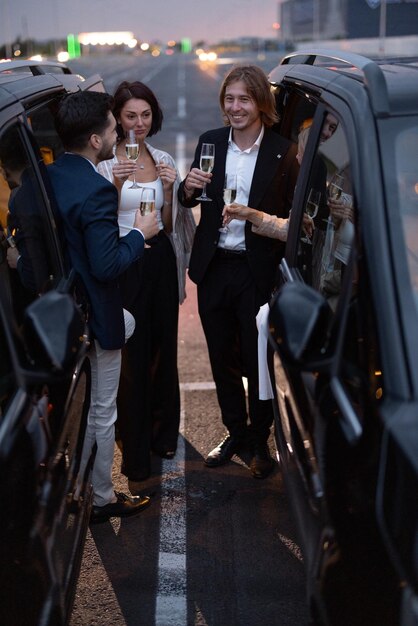 Photo un groupe de partenaires commerciaux s'amuse ensemble en buvant de l'alcool tout en célébrant entre les voitures sur le parking la nuit