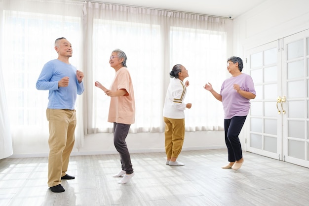 Un groupe de personnes âgées asiatiques actives se mélangent avec des hommes et des femmes qui font de l'exercice en dansant ensemble à la maison avec des sourires et des rires relaxants Activité intérieure pour les personnes âgées matures et les retraités