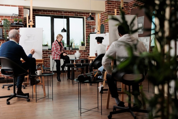 Groupe de personnes de différents âges apprenant à dessiner des objets de nature morte avec un artiste professionnel, assistant à un cours d'art en groupe, étudiants assis en classe dessinant avec un crayon sur toile