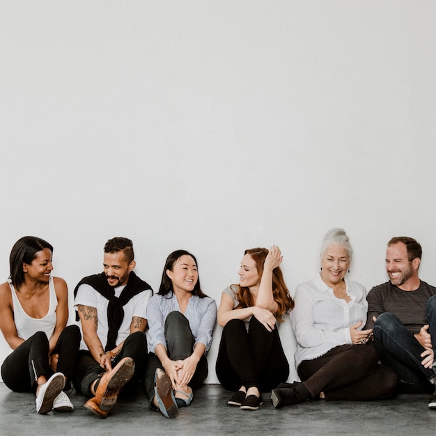 Groupe de personnes diverses et joyeuses assises sur un sol dans une salle blanche