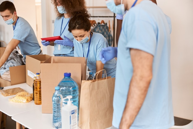 Groupe de personnes diverses portant des masques de protection et des gants uniformes bleus triant les produits alimentaires donnés