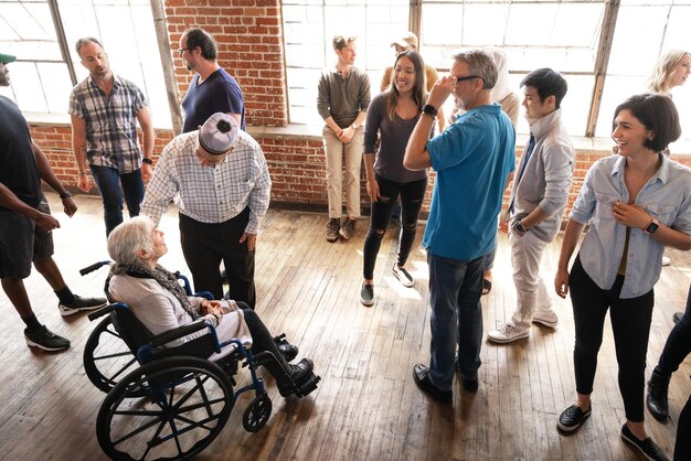 Groupe de personnes diverses socialisant dans une pièce lumineuse Comprend une femme âgée en fauteuil roulant tenue décontractée atmosphère amicale Une femme âgée dans un fauteu il roulant entourée de la communauté et du soutien