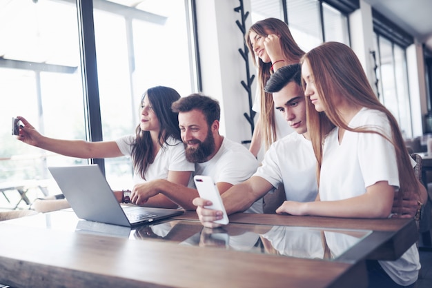 Un groupe de personnes fait une photo de selfie dans un café. Amis et étudiants se sont réunis autour de l'ordinateur portable et préparent un projet commun