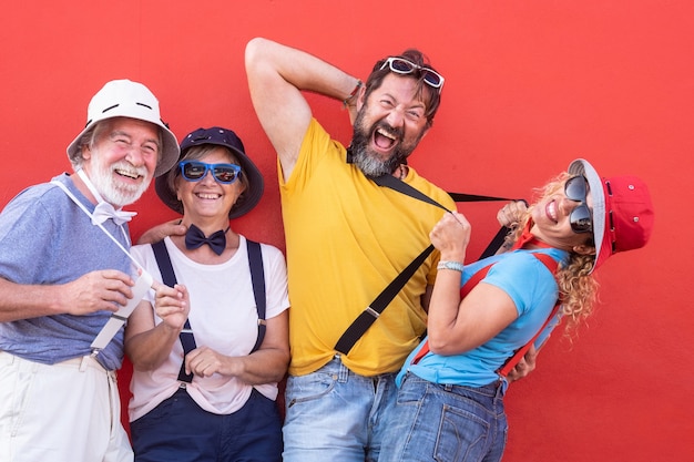 Groupe de personnes heureuses adultes âgées et d'âge moyen jouant en plein air contre un mur rouge. Habillé en tailleur avec nœud papillon et bretelles. Plein de couleurs, fête ou jour de fête