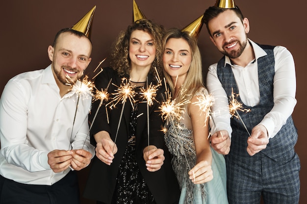 Groupe de personnes heureuses portant des chapeaux de fête tenant des étincelles brûlantes pendant les vacances ou la célébration d'un événement