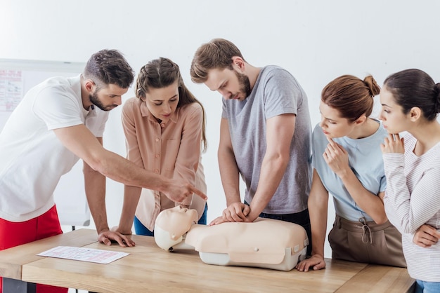 Groupe de personnes avec un instructeur exécutant la RCR sur un mannequin pendant la formation aux premiers secours