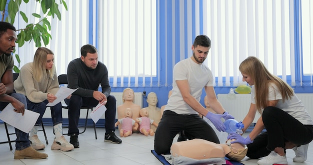 Groupe de personnes avec instructeur pratiquant la RCR sur mannequin lors d'un cours de premiers soins à l'intérieur.