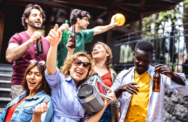 Groupe de personnes multiculturelles s'amusant à applaudir avec une boombox et une bouteille de bière Amis d'âge mixte profitant ensemble du festival de vacances de printemps Concept de style de vie des jeunes sur un filtre vif et lumineux