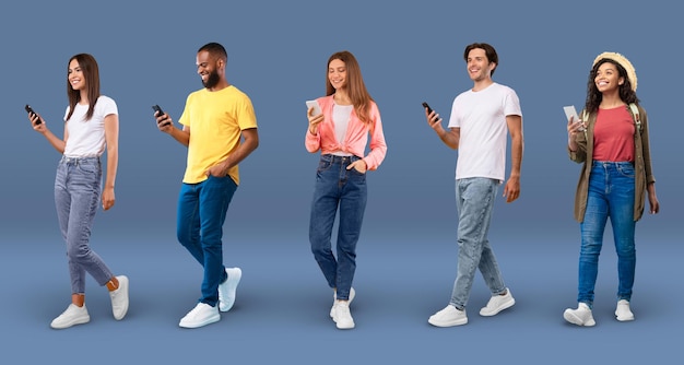 Groupe de personnes multiethniques heureuses avec des smartphones marchant sur fond bleu