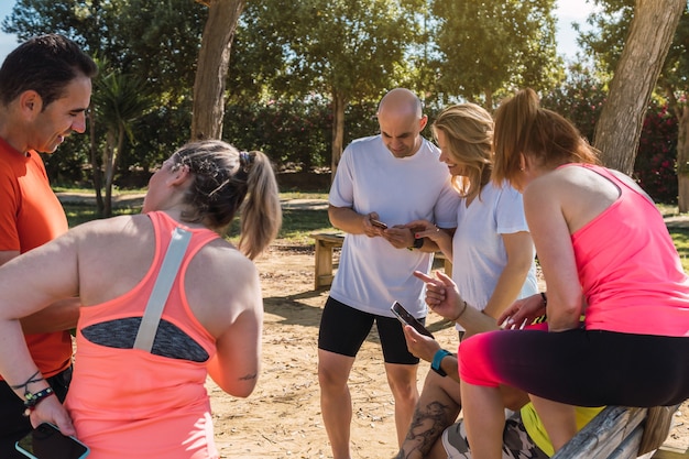 Photo groupe de personnes en tenue de sport utilisant le mobile tout en parlant dans un parc
