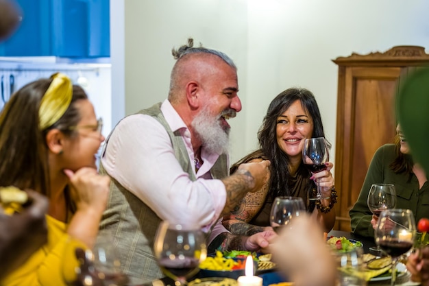 Groupe de personnes végétariennes s'amusant lors d'un dîner à la maison privée se concentrant sur la femme brune pointée par un homme barbu hipster d'âge mixte amis s'amusant à boire du vin en mangeant des aliments sains