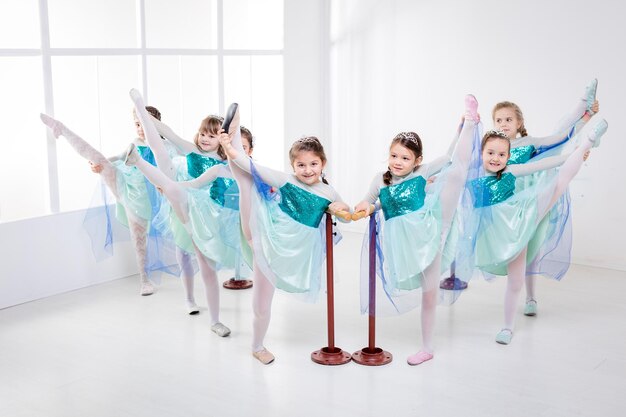 Groupe de petites filles souriantes utilisant la barre tout en pratiquant dans un studio de danse.