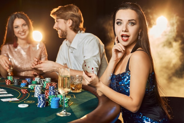 Groupe d'un peuple élégant jouant au poker à la maison de jeu. Focus sur une luxueuse brune vêtue d'une robe bleue brillante