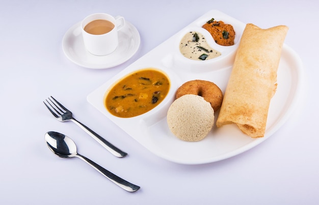 Groupe de plats indiens du sud dosa, idli ou oisif, vada, chutney de noix de coco sambar et thé chaud, plateau de variétés sud-indien