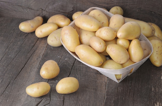 Groupe de pommes de terre crues sur une planche rustique et dans un petit plateau