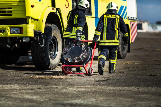 Groupe de pompiers en casque sûr et uniforme debout en voiture