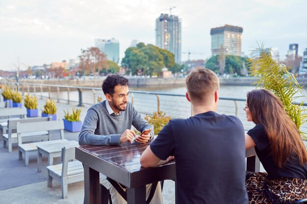 groupe de portraits d'amis assis dans un bar à l'extérieur en train de parler en souriant