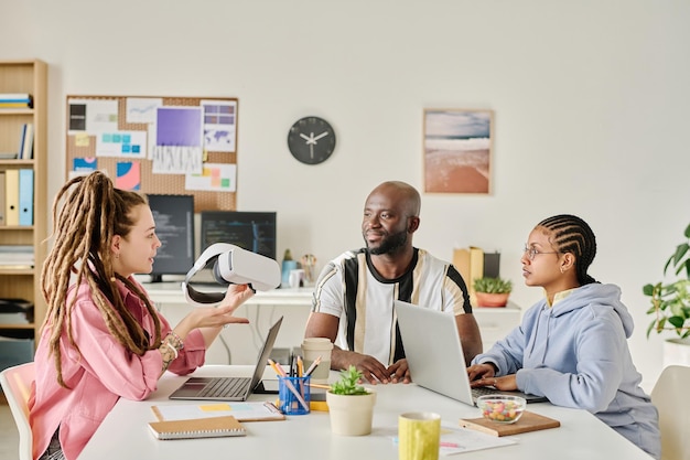 Groupe de programmeurs discutant d'un nouveau gadget à table en équipe lors d'une réunion au bureau informatique