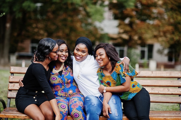 Groupe de quatre filles afro-américaines assises sur un banc en plein air et câlins