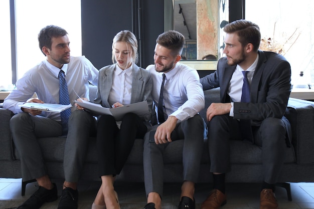 Groupe de quatre hommes d'affaires assis sur un canapé. Ils ne pourraient pas être plus heureux de travailler ensemble.