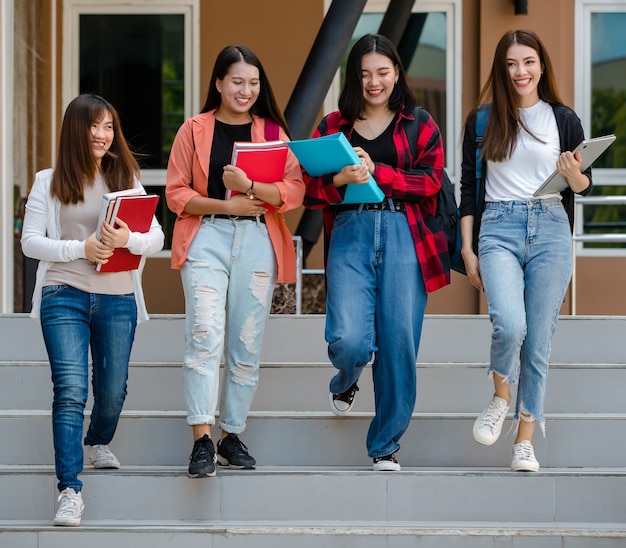 Groupe de quatre jeunes étudiantes asiatiques séduisantes marchant ensemble sur le campus universitaire parlant et riant de joie. Concept pour l'éducation et la vie des étudiants.