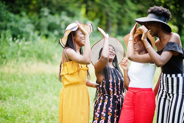 Groupe de quatre magnifiques femmes afro-américaines portant un chapeau d'été passant du temps à l'herbe verte dans le parc