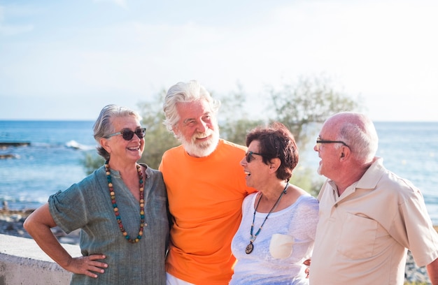 Groupe de quatre personnes âgées et matures avec une amitié à la plage parlant et profitant ensemble - mer à l'arrière-plan