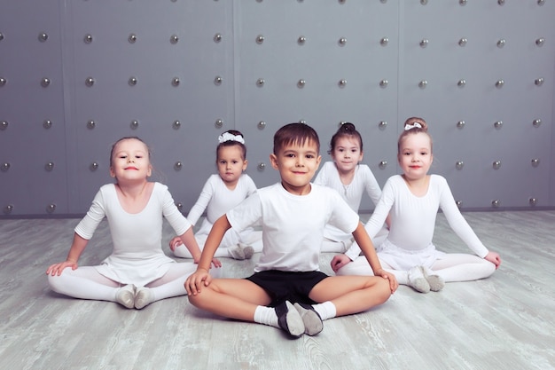 Groupe de quatre petites ballerines et ballerine enfant posant ensemble et pratiquant