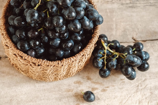 Groupe de raisins noirs dans un panier en osier rond sur une vieille table en bois