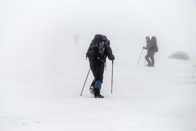 Groupe de randonnée en montagne avec sacs à dos et bâtons de randonnée ayant un voyage d'escalade difficile dans la tempête de neige hivernale