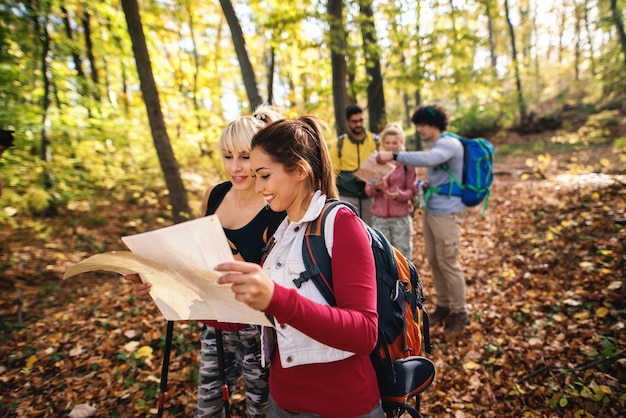 Groupe de randonneurs regardant la carte dans les bois à l'automne. Au premier plan, deux femmes regardant la carte et en arrière-plan le reste du groupe.