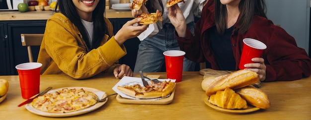 Groupe riant de jeunes femmes diverses traînant ensemble à la maison et mangeant de la pizza