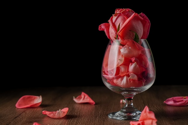 Un groupe de roses roses dans un verre à vin qui tombe sur une table en bois de couleur foncée