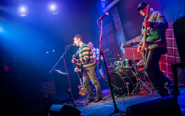 Le groupe se produit sur scène, concert de musique rock dans une discothèque. Prise de vue authentique avec une iso élevée dans des conditions d'éclairage difficiles. Un peu de grain et des effets de mouvement flou.