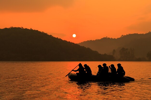 Photo un groupe de soldats aide à ramer un bateau pour cibler le crépuscule, la montagne et le soleil en arrière-plan.