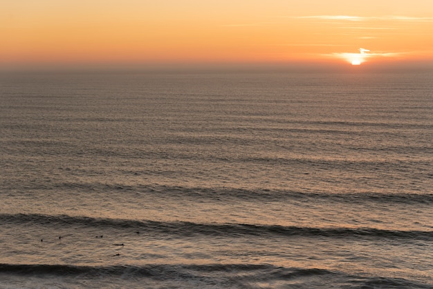 Groupe de surfeurs en attente d&#39;une vague au milieu de la mer avec le soleil au crépuscule en arrière-plan