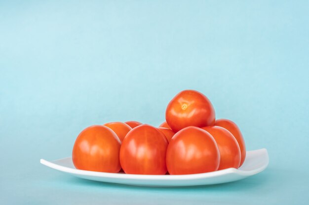 Groupe de tomates fraîches sur plaque blanche sur fond bleu. Gros plan stock photo