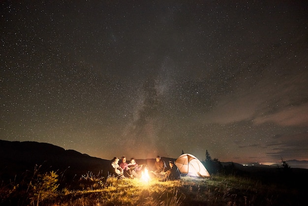 Groupe de touristes avec guitare en brûlant un feu de joie sous un ciel étoilé sombre avec la constellation de la Voie lactée.