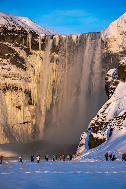 Groupe de touristes s'émerveillant et prenant des photos de la gigantesque cascade enneigée de Skogafoss complètement