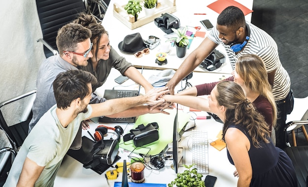 Groupe de travailleurs de démarrage de jeunes employés empilant les mains au studio urbain pendant le projet de remue-méninges de l'entrepreneuriat