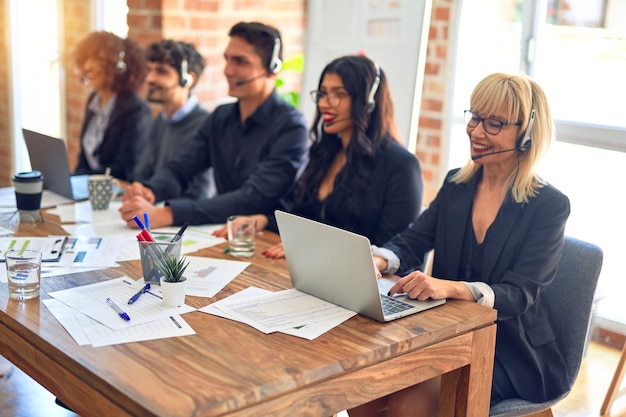 Groupe de travailleurs du centre d'appel souriant heureux et confiant. Travailler avec le sourire sur le visage à l'aide d'un casque au bureau.