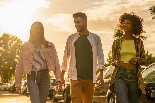 Groupe de trois jeunes marchant avec le coucher du soleil derrière des moments d'été de détente et de vacances de la génération z