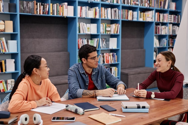 Groupe de trois jeunes qui étudient ensemble dans une bibliothèque universitaire moderne